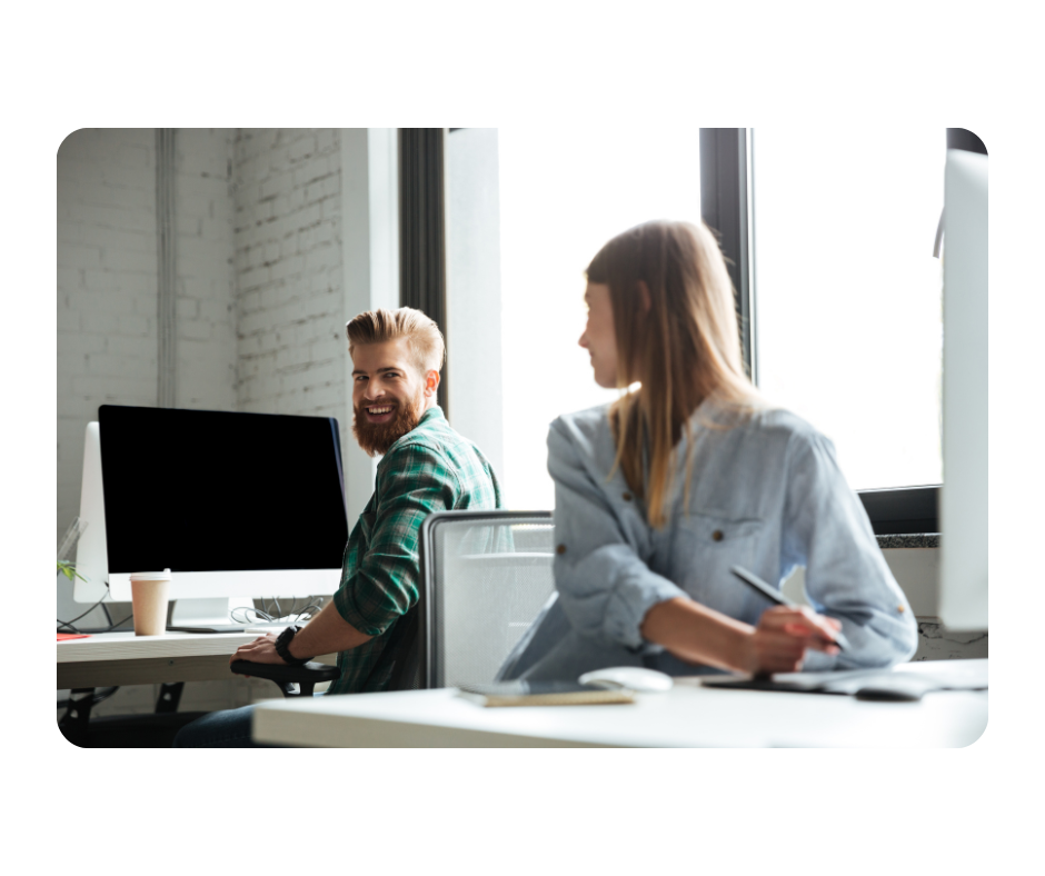 Young people smiling at each other in office while both work on their computers