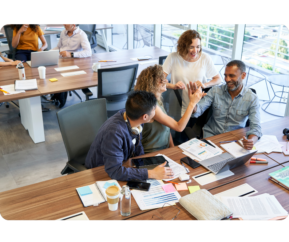 Four people in office smiling and working on a desk in front of computers
